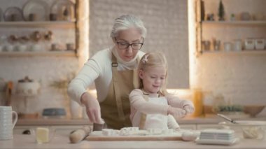 Noel tatilleri. Büyükannem ve küçük kızım mutfakta. Kurabiyelerine un serpiyorlar. O zaman Unu Ellerinden Çalkala. Kızın kafasında sarı saç ve süslemeler var.