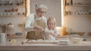 Noel tatilleri. Büyükannem ve küçük kızım mutfakta. Arkalarında teçhizatlı bir sürü raf var. Kız, farklı şekillerde hamur şekline bürünüyor. Noel kurabiyesi yapıyorlar. Büyükanne Servis
