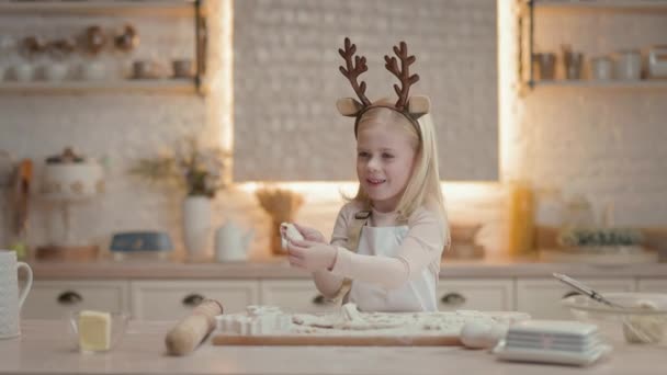 4人のかわいい女の子は生地からクッキーを作ります キッチンで小さな女の子クリスマスクッキーを準備します 鹿の角の形で子供の頭の装飾に 新年とクリスマスの準備 — ストック動画