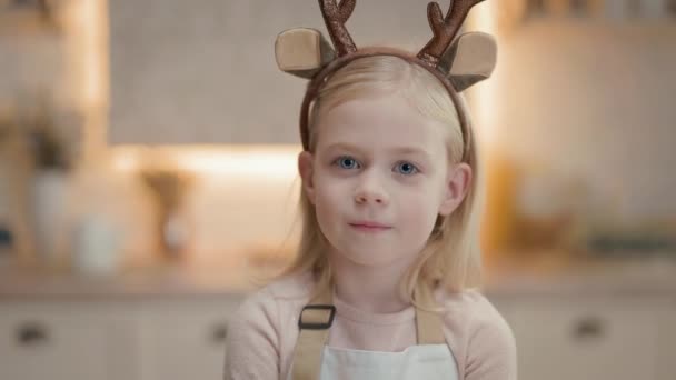 金髪のかわいい女の子の肖像画 彼女は4月に台所に立っている 頭には鹿の角の装飾が施されている 小さな女の子の笑顔 — ストック動画