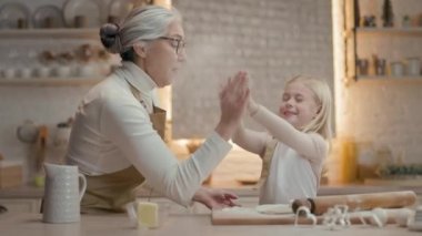 Noel tatilleri. Büyükannem ve küçük kızım mutfakta. Önlüklü yeni yıl pastası hazırlıyorlar. Kızın kafasında geyik boynuzu şeklinde sarı saç ve süslemeler var. Büyükanne ve Kız