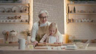 Noel tatilleri. Büyükannem ve küçük kızım mutfakta. Arkalarında teçhizatlı bir sürü raf var. Noel kurabiyesi yapıyorlar. Büyükannem Kız 'ın arkasında duruyor. Yuvarlak Pin ve Diz tutuyorlar
