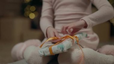 Kız Noel Hediyesini Açıyor. Arkasında Noel ağacı çelenklerle parıldıyor. Görünmez yüz. Hediyeyi Açmaya Çalışan Çocuk.
