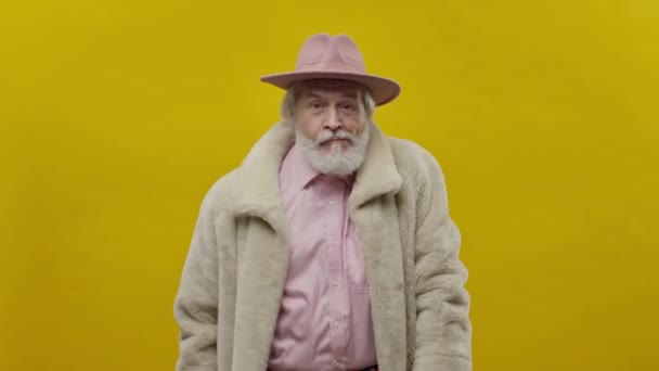 穿着粉色衣服的古板老人背景是黄色的 他是灰色与胡子和胡子 他头上顶着一只帽子 — 图库视频影像