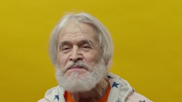 髭を生やした老人の肖像画 黄色の背景に灰色の男 彼は自分の顔に異なる感情を表現する — ストック動画