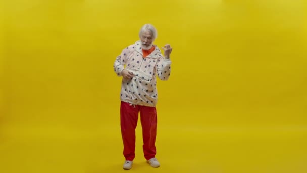 一个留着胡子的老人的画像 黄种人背景 穿着红裤和星光夹克的时髦男人 他的表情很严肃 他在黄色背景上显得矮小 — 图库视频影像
