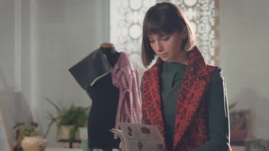 Stüdyoda Duran Genç Kız. Dergiye göz atıyor. Kısa saçlı, uzun ceketli hoş bir kadın. Odada bir sürü resim ve kolaj var. Yaratıcı Stüdyo. Elbiseli ve Dikişli Manken