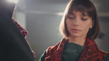 Stüdyoda Genç Kız. Kısa saçlı, uzun ceketli hoş bir kadın. Odada bir sürü resim ve kolaj var. Yaratıcı Stüdyo. Giysileri ve dikiş aksesuarları olan bir manken. Giyinmeye Çalışan Kadın