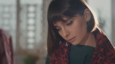 Stüdyoda çalışan genç kız moda tasarımcısı. Odaklanmış durumda. Kısa saçlı, uzun ceketli tatlı kız..