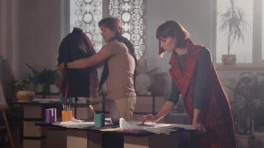 Stüdyoda Genç Kadın ve Erkek Tasarımcılar. Kısa saçlı güzel bir kadın ve boynunda fular olan bir adam. İş akışı. Çalışmayı tartışıyorlar. Kadın dizüstü bilgisayarda çalışıyor ve erkek santimetreyle mankeni ölçüyor