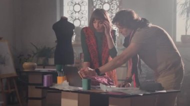 Stüdyoda Genç Kadın ve Erkek Tasarımcılar. Kısa saçlı güzel bir kadın ve boynunda fular olan bir adam. İş akışı. Çalışmayı tartışıyorlar. Adam Bilgisayarda Bir Şey Gösteriyor.