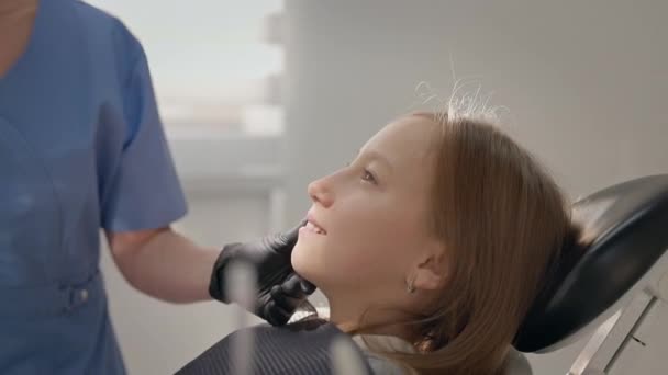 歯医者試験 歯科医の椅子に座ってかわいい女の子 若い女性医師は女の子の顔に触れます 彼女は女の子の顔に光を指示します — ストック動画