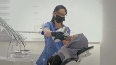 Ofiste çalışan dişçi. Yakındaki genç hastanın yüzü. Kafasında atkısı olan genç bir kız dişçi koltuğunda oturuyor. Genç Maskeli Kadın Doktor Kadın Hastaya Röntgen Çekti.