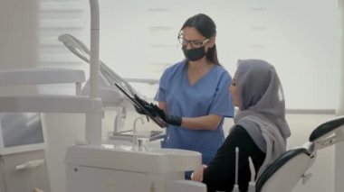 Ofiste çalışan dişçi. Yakındaki genç hastanın yüzü. Kafasında atkısı olan genç bir kız dişçi koltuğunda oturuyor. Genç Kadın Maskeli Doktor Hasta Xray 'ini Gösteriyor.