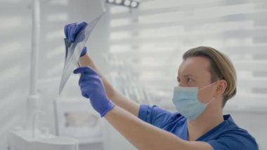 Genç Doktor Diş Hekimliği Ofisi 'nde. Tıbbi Maskeli Doktorlar Yüzü. Doktor Xray 'i muayene ediyor. Onu tutuyor ve ışığa yoğun bir şekilde bakıyor..