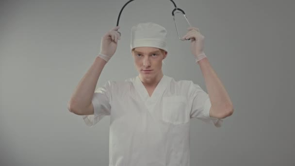 医療用ガウンと手袋の若い医師 かわいい男は灰色の背景に立って — ストック動画