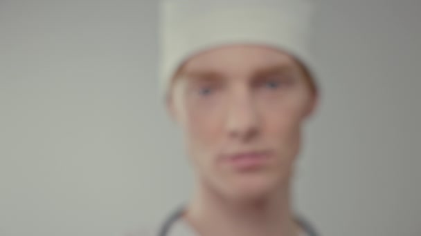 若い医者の顔 彼は顔の前で彼の手にアンプルを保持します 白い帽子の若い白人男性 手には医療用手袋 — ストック動画