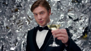 Şampanya kadehleriyle parlak arka planda genç bir adam. Takım Elbiseli Şirin Adam. Parti.