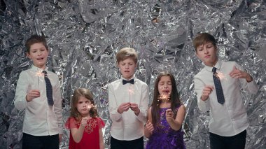 Gümüş Sahne Arkaplanındaki Beş Çocuk. Kutlama. Üç Oğlan ve İki Kız. Neşeli Çocuklar. Maytap tutuyorlar. Beyaz tişörtlü erkekler ve elbiseli kızlar..