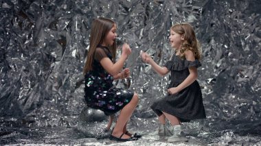 Parlak Arkaplanda İki Kız. Şenlik Elbiseli Kızlar. Parlak katmanlarda oturan ve gülümseyen kızlar. Çocuklar eğlensin..