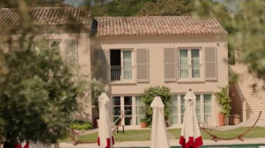 Small Old House With Shutters On Windows. Beautiful Summer Day. Sun Umbrellas Are Stacked In Yard.