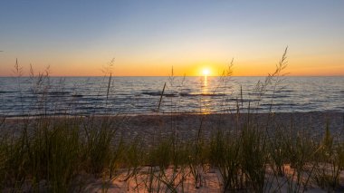 Michigan Gölü 'nde uzun kum tepecikleri, gölün üzerinde günbatımı arka planıyla.