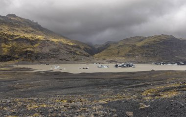 Floating ice in the river at Solheimajokull glacier in southern Iceland, surrounded by mountains.