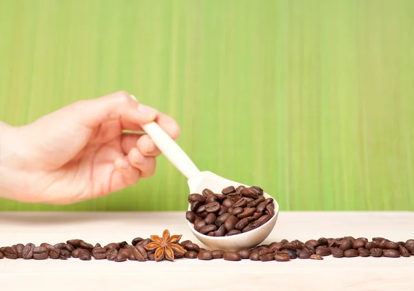 Kávová zrna na dřevěný stůl s dřevěnou lžící — Stock fotografie