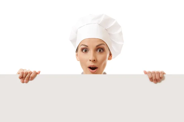 Vrouw kok kijkt uit over papier teken billboard. — Stockfoto