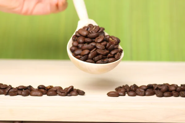 Kávová zrna na dřevěný stůl se lžičkou — Stock fotografie