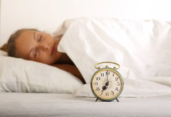 Mujer joven dormida y despertador en la cama — Foto de Stock