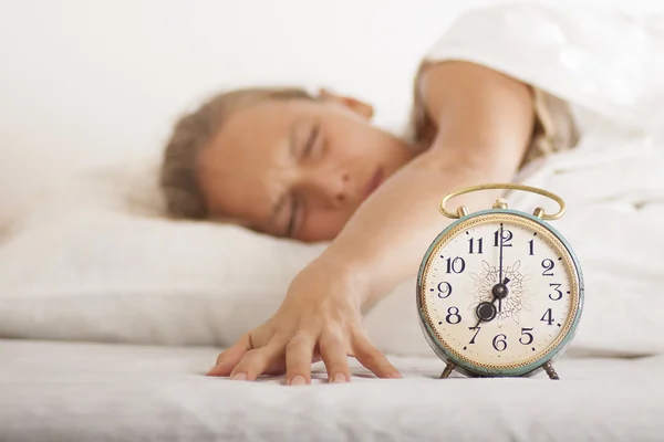 Mujer joven dormida y despertador en la cama — Foto de Stock