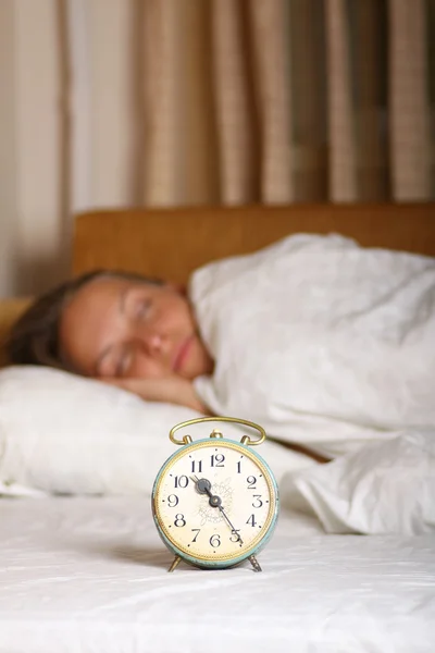 Genç kadın ve çalar saat yatakta uyuyor — Stok fotoğraf