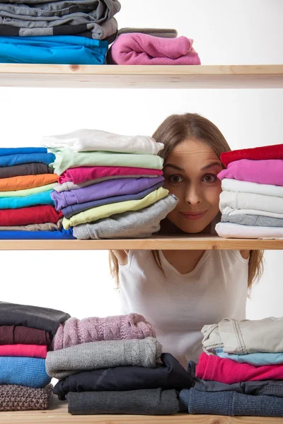 Young woman hiding behind a shelf with clothing — Stock Photo, Image