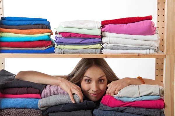 Young woman hiding behind a shelf with clothing — Stock Photo, Image