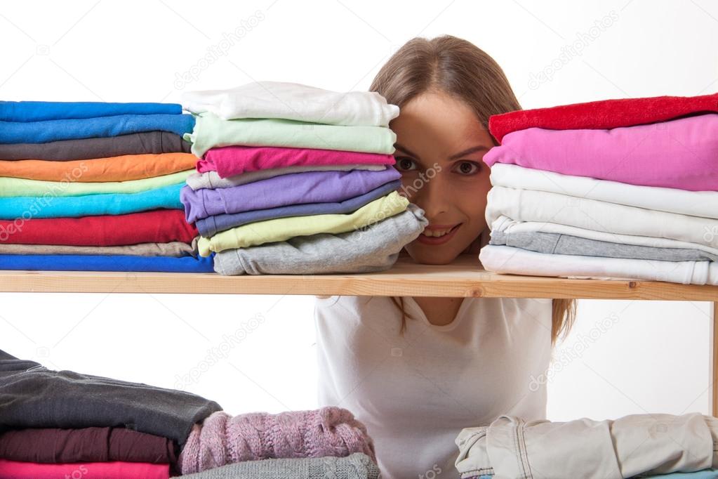 Young woman hiding behind a shelf with clothing