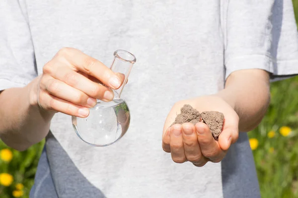 Dry soil in hand and a flask with water — Stock Photo, Image
