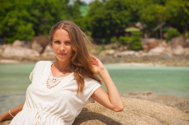 Deniz kenarında bir kayanın üzerine oturmuş elbiseli kız