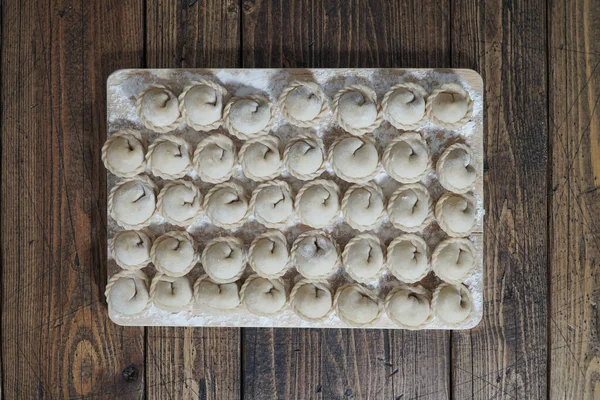 Fleisch oder vegetarische Klöße, Pelmeni auf einem Holzbrett. Russisches Nationalgericht. Ansicht von oben. — Stockfoto