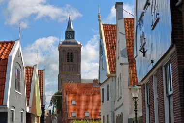 De Rijp, Alkmaar, Kuzey Hollanda, Hollanda 'daki renkli ve tarihi evlerin cephelerinde Grote Kerk kilisesinin saat kulesi var. De Rijp, Kuzey Hollanda 'nın en eski ahşap evlerinden bazılarının yer aldığı rijksanıtlarıyla tanınır.