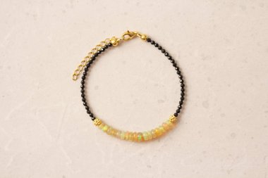 Siyah bilezik, ateş opal bileziği. Doğal taşlardan yapılmış bir bilezik. Siyah dönüş, ateş opalı. Doğal taşlardan yapılmış el yapımı mücevherler. Hafif, modern beton arka planda modern mücevherler.