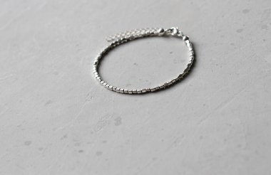 Küçük gümüş boncuklardan yapılmış gümüş bir bilezik. Yazarın şık ve modern mücevherleri. Hafif modern arka planda metal gümüş boncuklardan yapılmış bilezik..