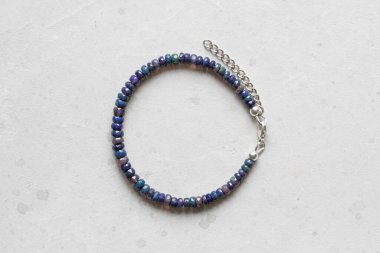 Siyah ateş opal bileziği. Eldeki taşlardan yapılmış bilezik. Siyah Ateş Opal 'den. Doğal taşlardan yapılmış bilezik. El yapımı mücevherler. Hafif modern arkaplanda el yapımı bilezikler.