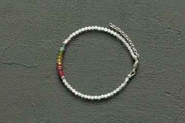 Çok renkli parlak bir turmalin, ay taşı bileziği siyah modern beton arka plana dayanıyor. Bileklik, eldeki taşlardan yapılmış. Siyah modern arka planda el yapımı bilezikler. LGBT bileziği.