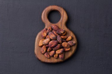 Kabuğu soyulmamış kahverengi kakao çekirdekleri ahşap tahtada, siyah arka planda yatıyor. Düz yat, maket yap, boşluğu kopyala. Kakao tozu, kakao içeceği ve çikolata yapmak için hammadde. Sağlık içeceği kavramı.