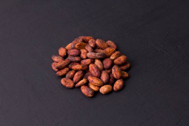 Soyulmamış çiğ kakao çekirdekleri siyah, modern beton arka planda yatıyor. Düz yat, maket yap, boşluğu kopyala. Kakao tozu, kakao içeceği ve çikolata yapmak için hammadde. Sağlık içeceği kavramı.