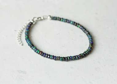 Siyah ateş opal el yapımı bileziği açık arkaplanda yatıyor. Doğal taşlardan yapılmış bilezik. Siyah ateş opalı. Doğal taşlardan yapılmış el yapımı mücevherler. Modern beton arka planda modern mücevherler.