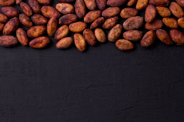 Soyulmamış çiğ kakao çekirdekleri siyah, modern beton arka planda yatıyor. Düz yat, maket yap, boşluğu kopyala. Kakao tozu, kakao içeceği ve çikolata yapmak için hammadde. Sağlık içeceği kavramı.