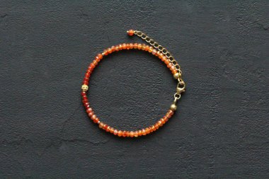 Doğal Carnelian ince bileziği. Doğal Carnelian taşlarından yapılmış bilezik. Doğal taşlardan yapılmış bilezik. El yapımı mücevherler. Siyah modern arka planda el yapımı bilezikler. Altın kaplama..