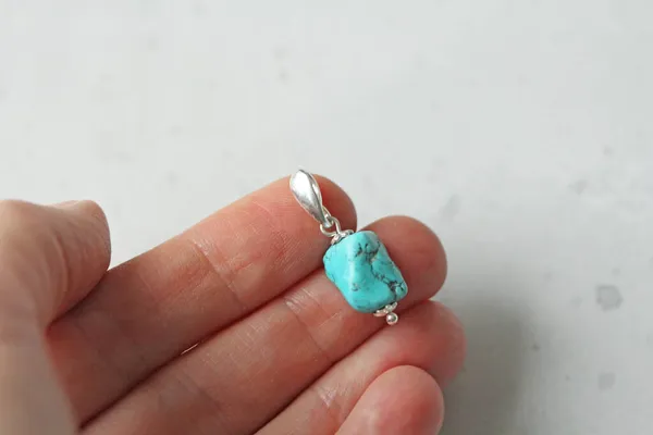A pendant made of natural stone Turquoise silver lies on a woman\'s hand. Author\'s jewelry from natural stones. Designer jewelry. On a light modern background. Natural minerals.